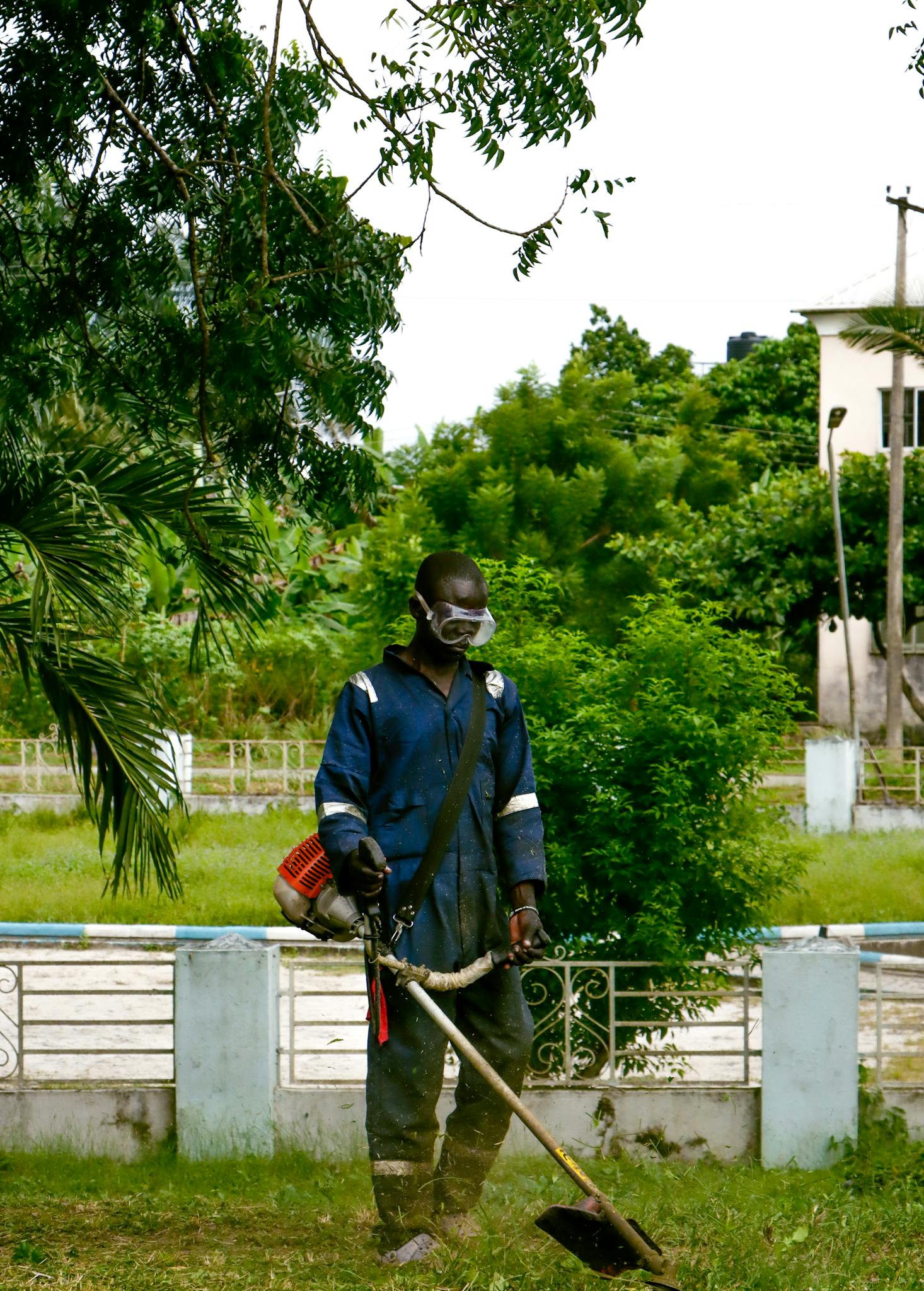 A man uses a grass trimmer in a vibrant outdoor park setting, surrounded by lush greenery.