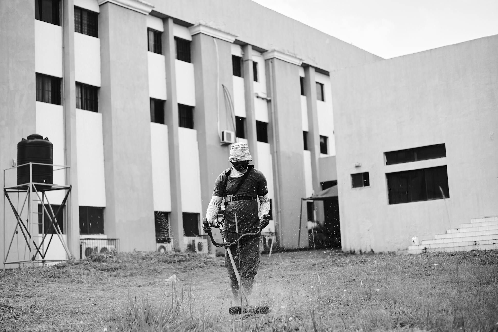 Man mowing lawn with trimmer in front of building, monochrome style.