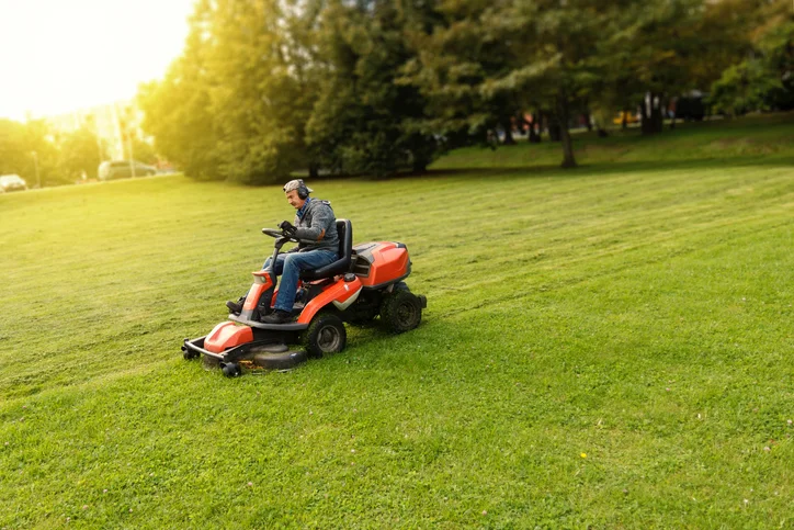 Lawn care technician mowing a green residential lawn with a commercial mower - lawn care service